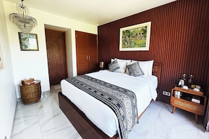 Un dormitorio con una cama grande, un armario de madera, una mesita de noche de mimbre y un cuadro enmarcado en la pared.