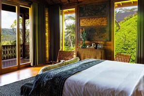 A bedroom with a large bed, a view of greenery, and a balcony.