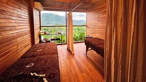A wooden room with two beds, a window with a view of greenery, and a hanging light fixture. - Aura Cemapaka (Karangasem)