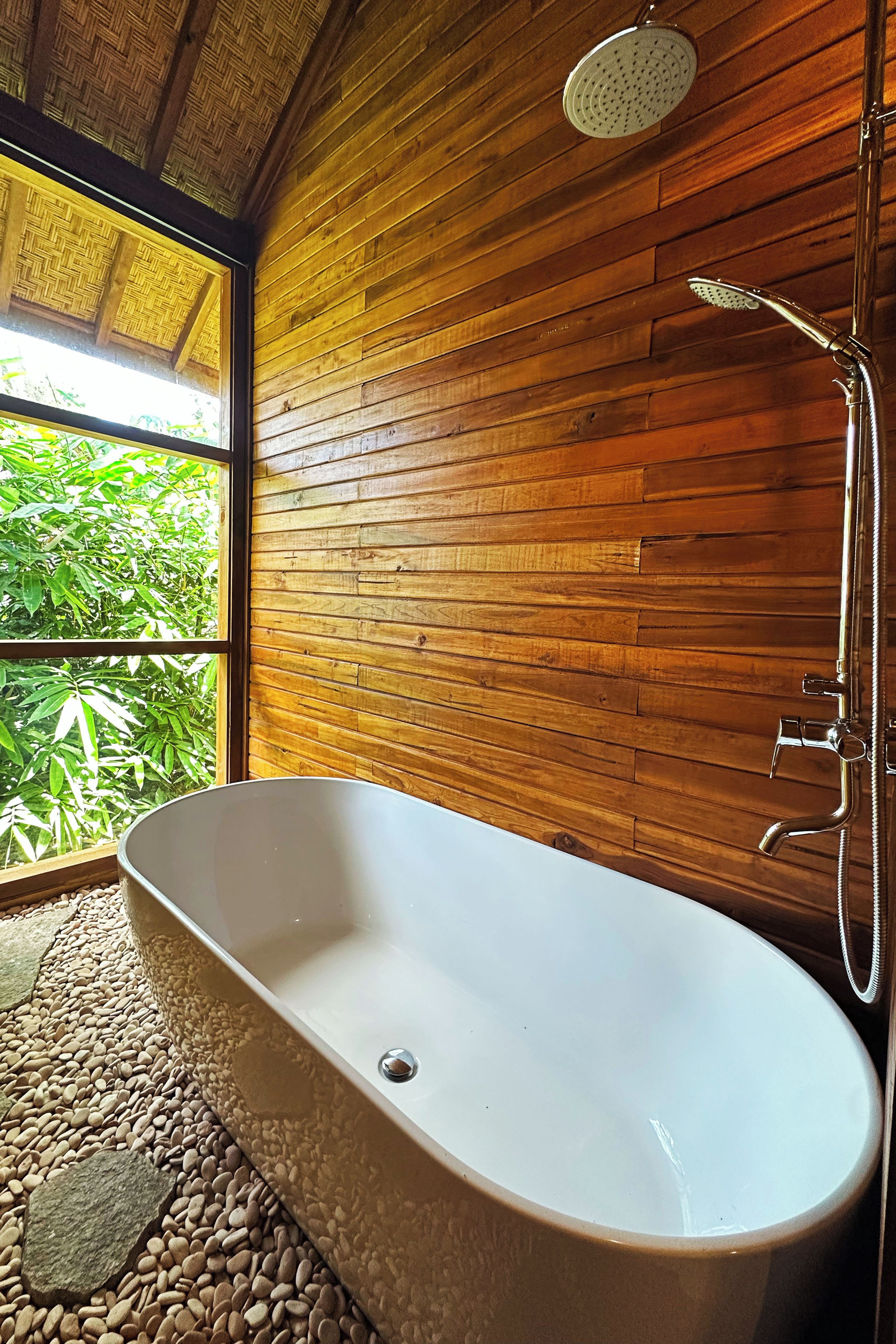 Un baño moderno con una bañera independiente, paneles de madera y vistas al exterior.