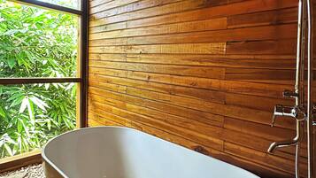 Un baño moderno con una bañera independiente, paneles de madera y vistas al exterior.