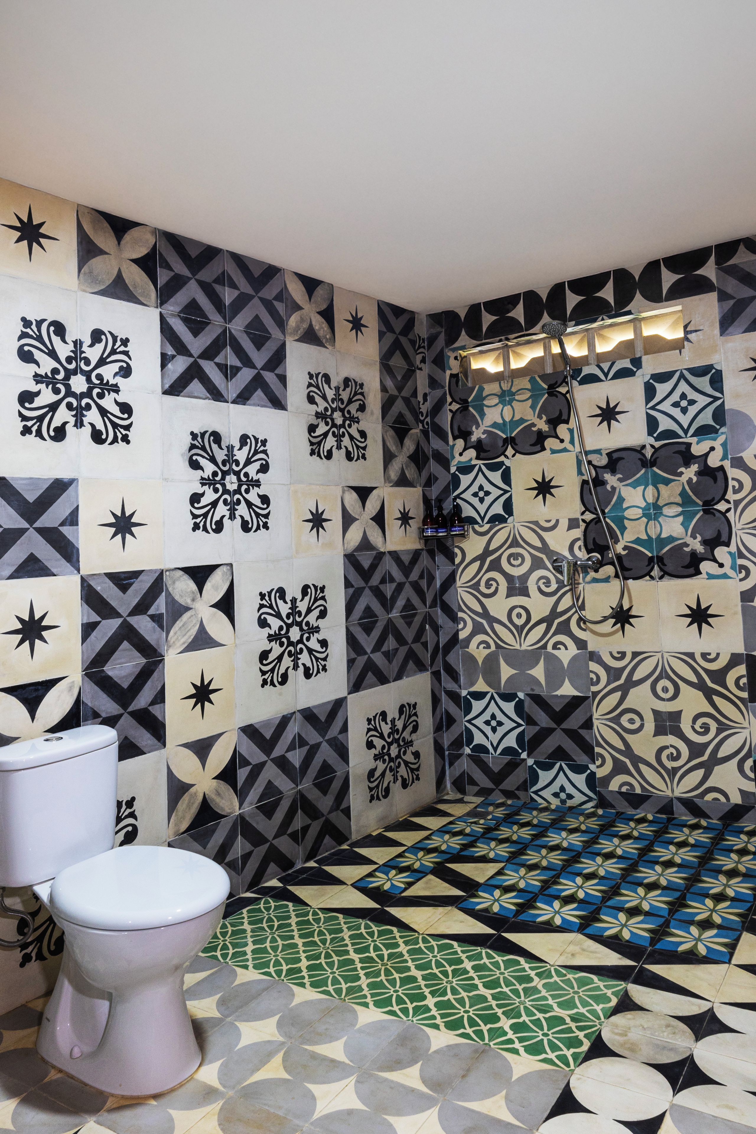 Une salle de bain comprenant des toilettes, un espace douche et un sol carrelé orné de motifs géométriques.