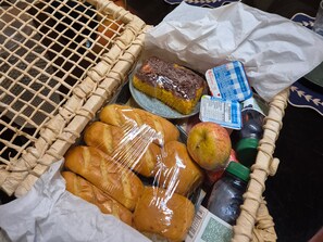 A wicker basket containing bread, a chocolate cake, a bottle of milk, and an apple.