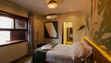 A hotel room with a bed, a window with curtains, a wall-mounted air conditioner, and a ceiling light fixture.