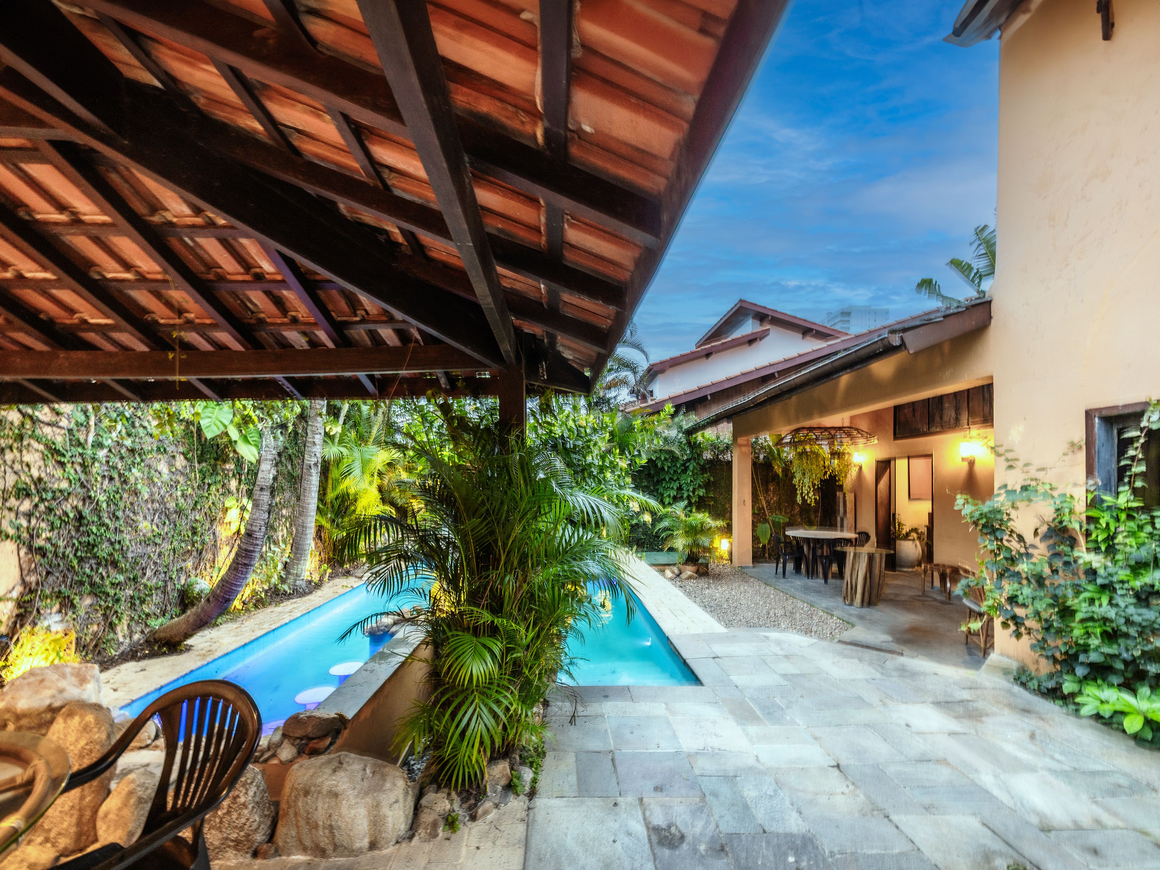 A covered outdoor area with a swimming pool, stone flooring, and a patio with seating.
