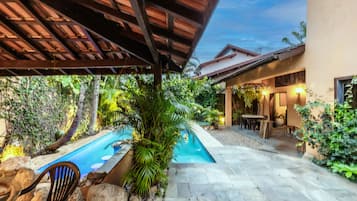 A covered outdoor area with a swimming pool, stone flooring, and a patio with seating.