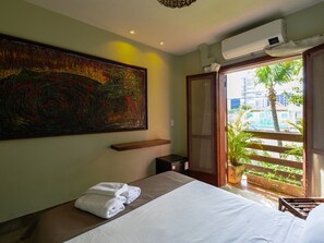 Ein Hotelzimmer mit einem Bett, einem großen abstrakten Gemälde und einem Balkon mit Blick auf Gebäude und Grünflächen.