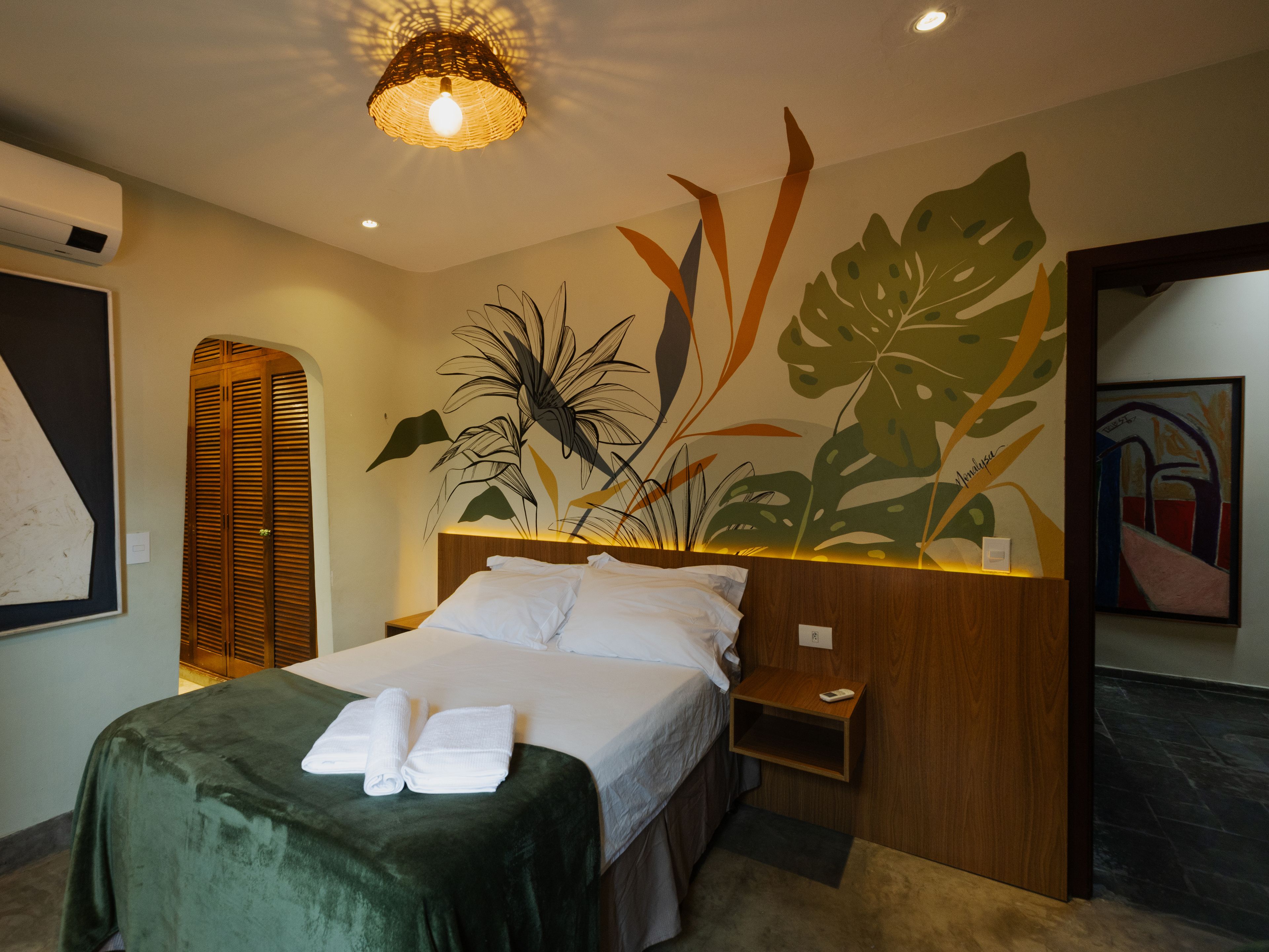 Une chambre d’hôtel avec un lit, une table de chevet, une étagère fixée au mur et une grande fenêtre.
