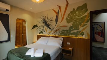 Habitación de hotel con cama, mesita de noche, estante en la pared y un ventanal grande.