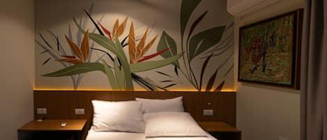 Habitación de hotel con una cama, dos mesitas de noche, un aire acondicionado de pared y un cuadro.