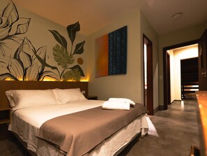 A hotel room with a large bed, a headboard with a plant design, a wall with a leaf pattern, and a door leading to a hallway.