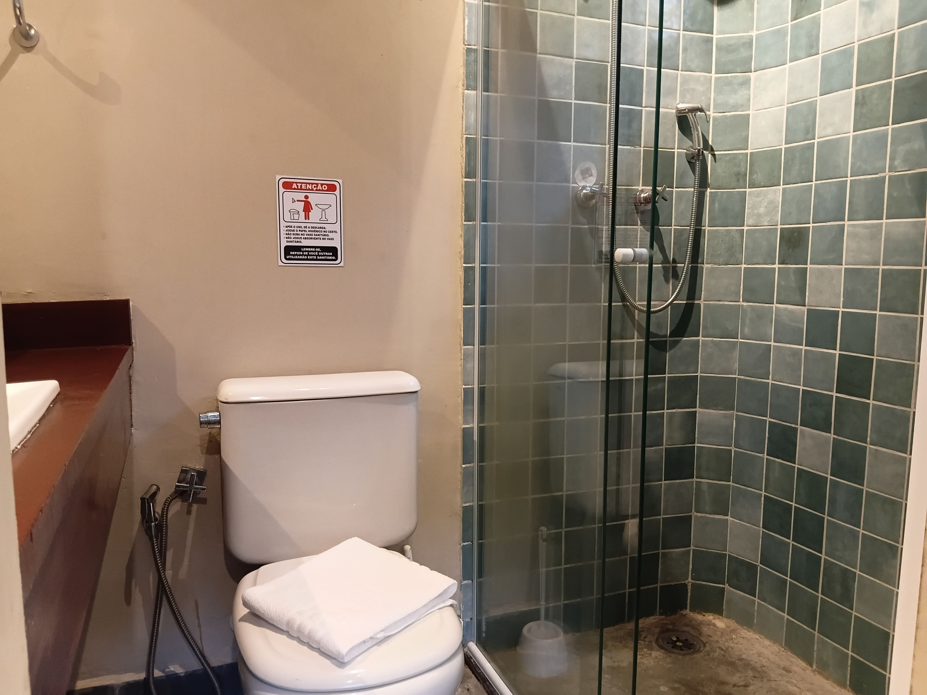 Un baño con inodoro, cabina de ducha de vidrio y un letrero de seguridad en la pared.