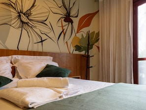 Una cama bien hecha con ropa de cama blanca y verde, un cabecero de madera y una pared con un mural floral.