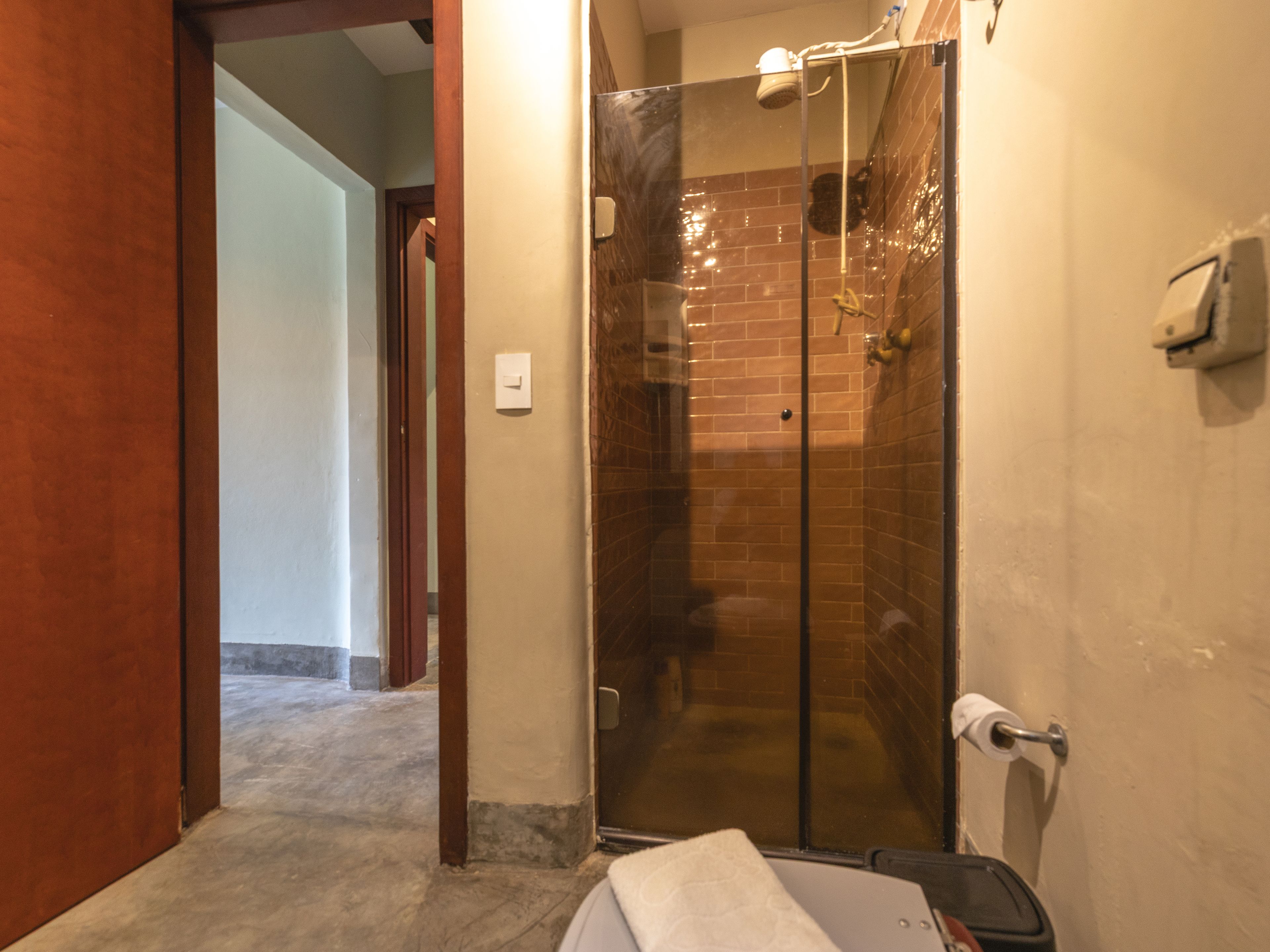 Un baño con cabina de ducha de vidrio, un perchero y un soporte para papel higiénico.