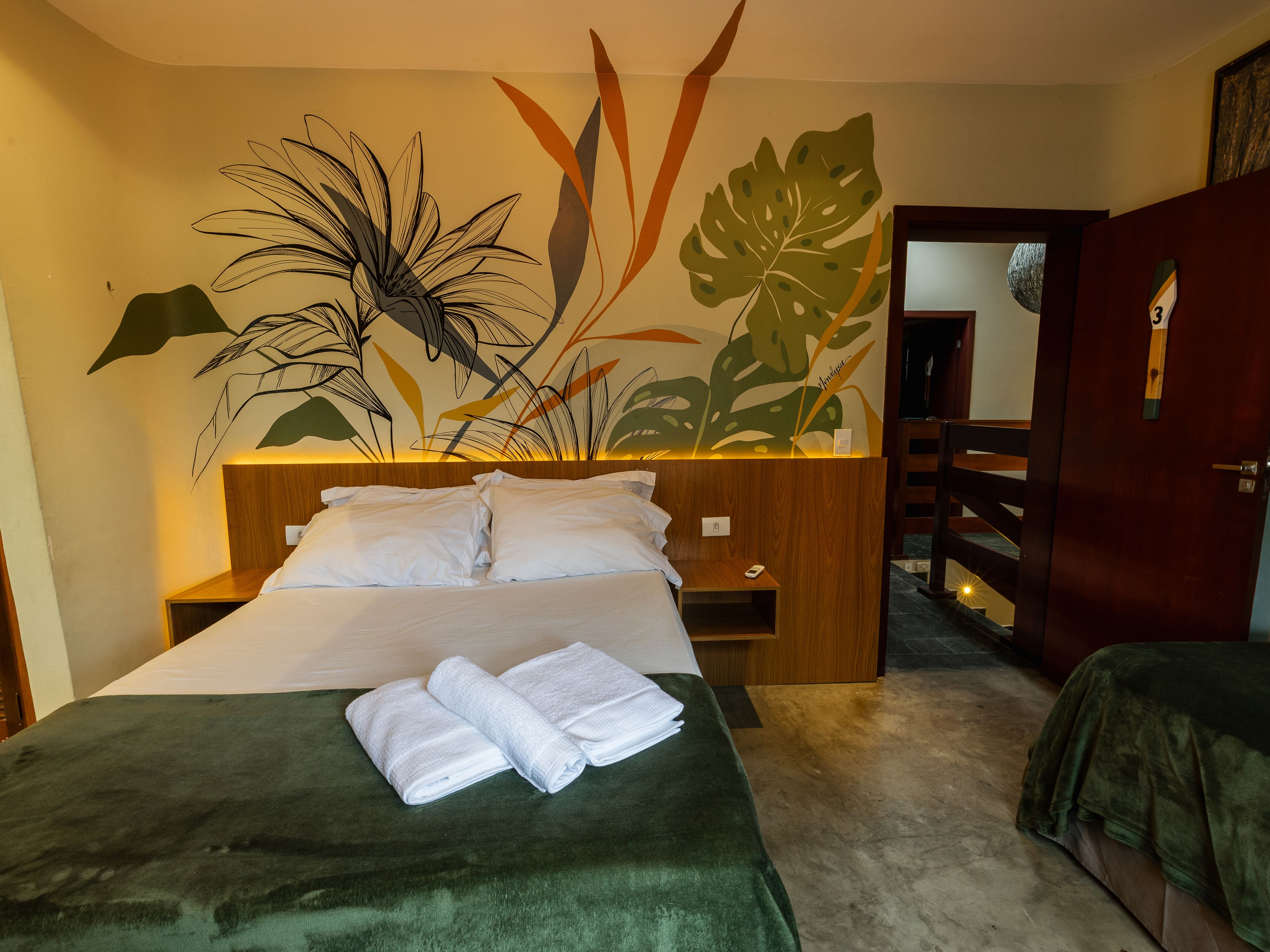A hotel room with a bed, a nightstand, a wooden headboard, and a wall mural.