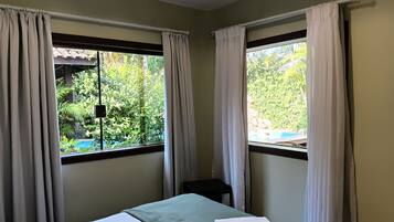 Habitación de hotel con cama, dos ventanas con cortinas, vista a zonas verdes y una piscina.