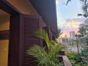 Une façade d’immeuble avec une porte et des volets en bois, un pot de fleurs et une vue sur le paysage urbain au coucher du soleil.