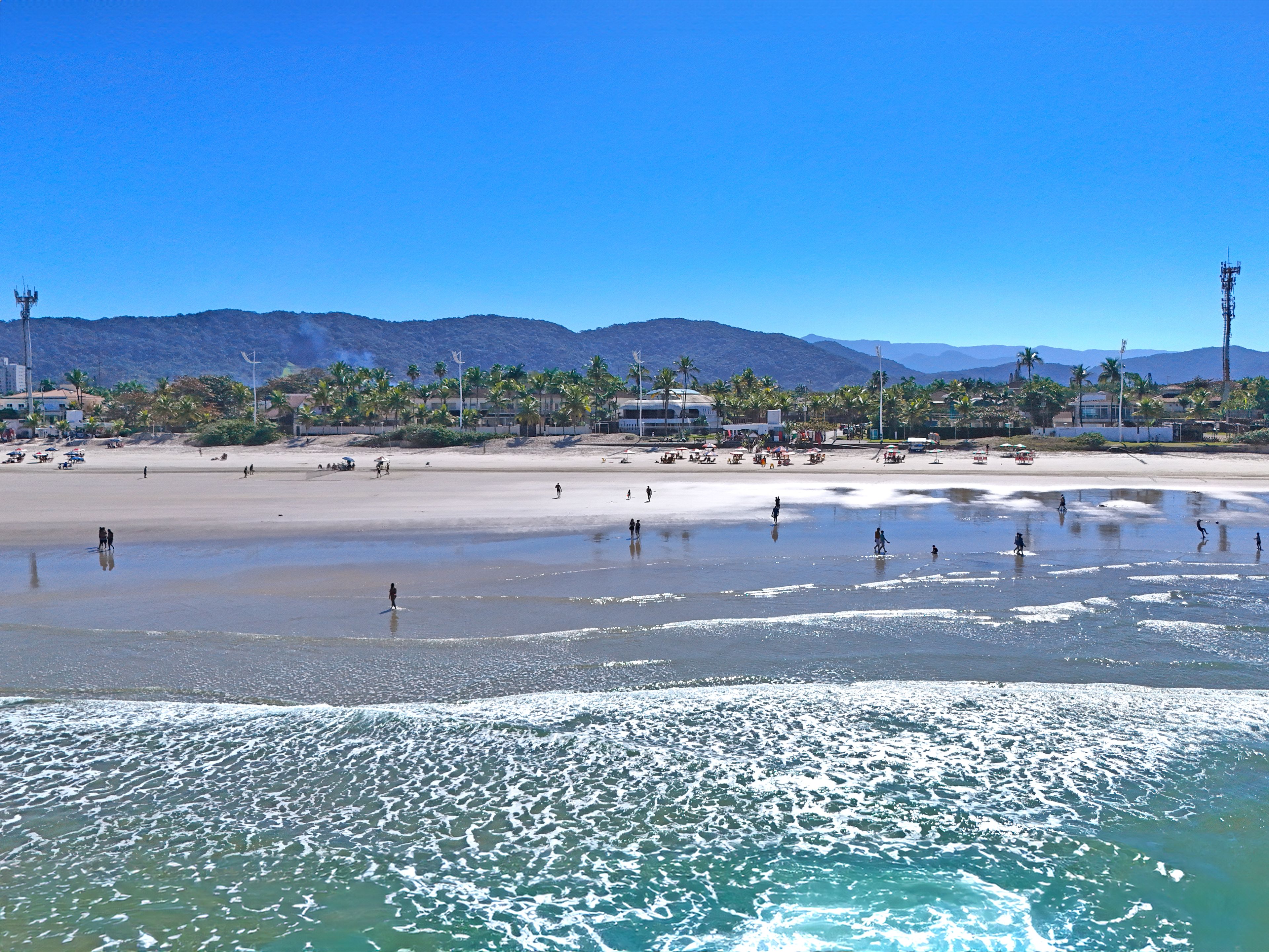 A beach with people, palm trees, and mountains in the background.