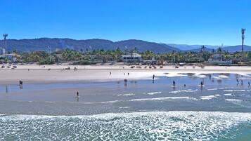 A beach with people, palm trees, and mountains in the background.