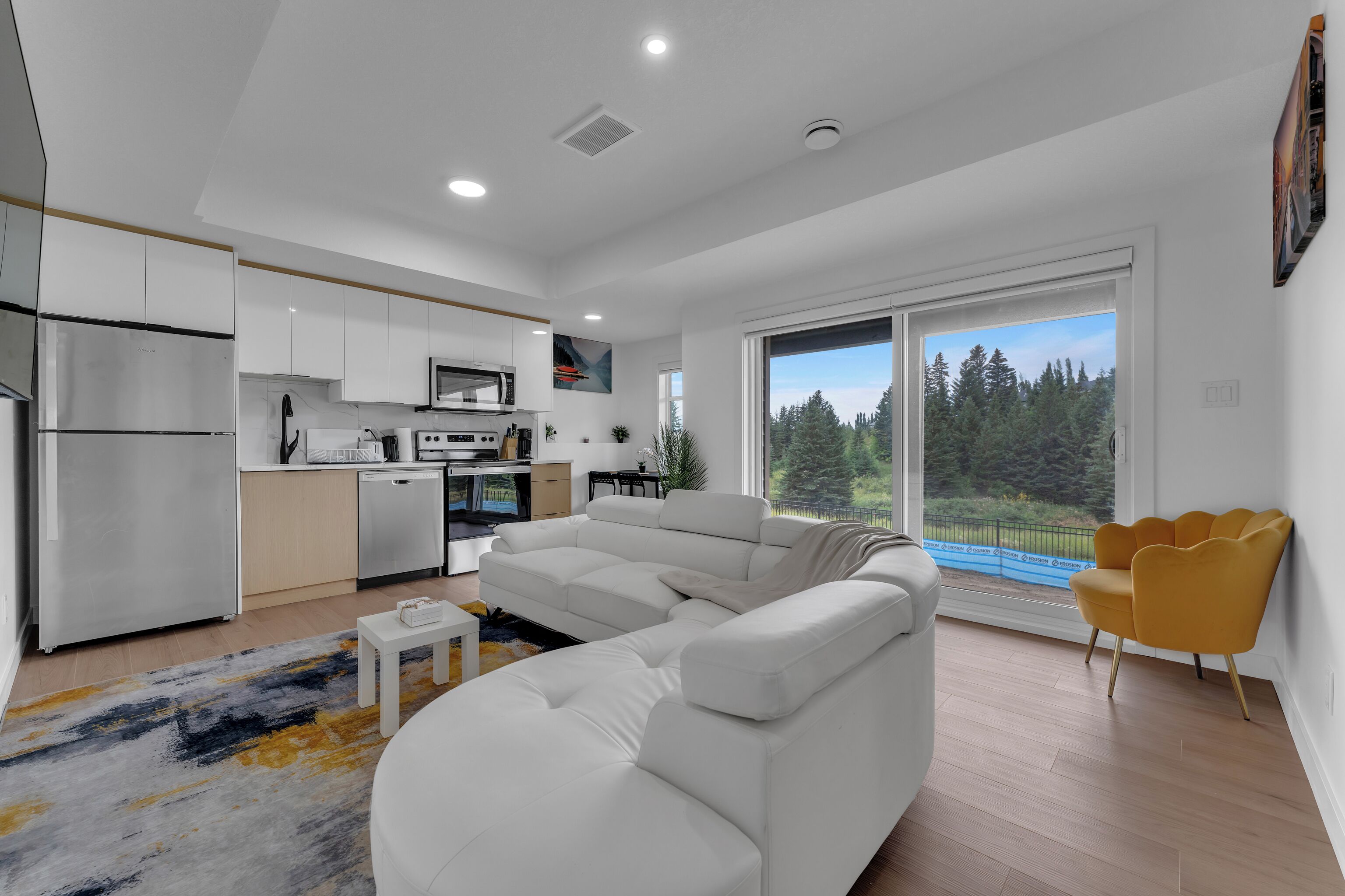 Una sala de estar moderna con un sofá blanco, una pequeña mesa de centro y vista a un bosque a través de amplios ventanales.