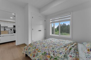 A bedroom with a bed, a window with a view of trees, and a kitchenette in the adjacent room. - Stylish 1BR Apartment | Close to YEG (Edmonton)