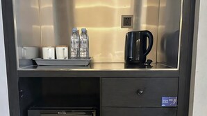 A compact kitchenette with a coffee maker, water bottles, and a small refrigerator.
