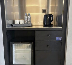 Una cuineta compacta amb cafetera, ampolles d'aigua i un refrigerador petit.