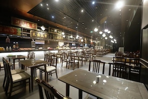 Un restaurante con varias mesas y sillas, una barra con productos alimenticios y luces colgantes.