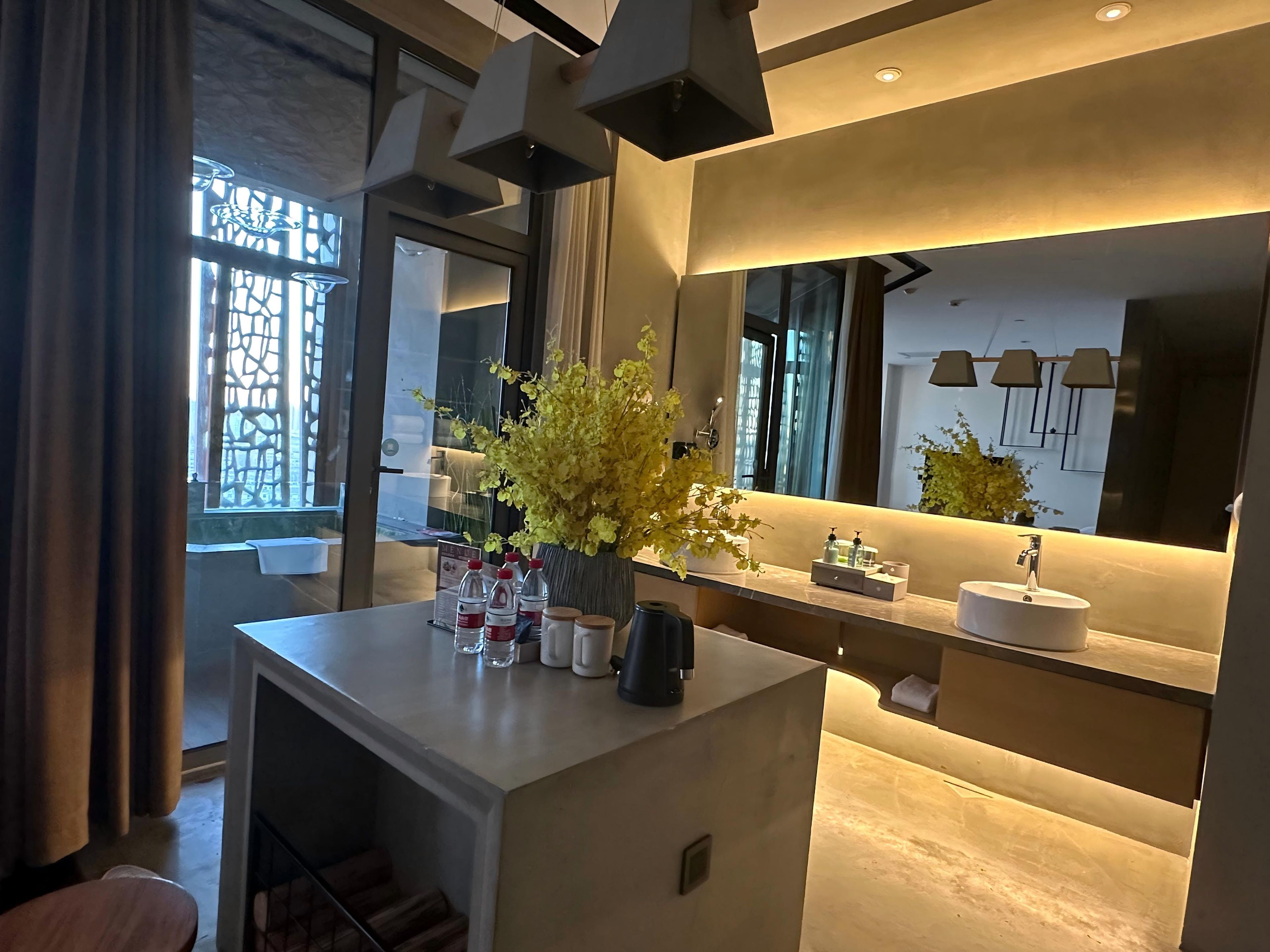 A modern bathroom with a large mirror, a sink, and a vase with yellow flowers.