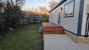 Un edificio moderno con una terraza de madera, un trampolín y un patio cubierto de césped.