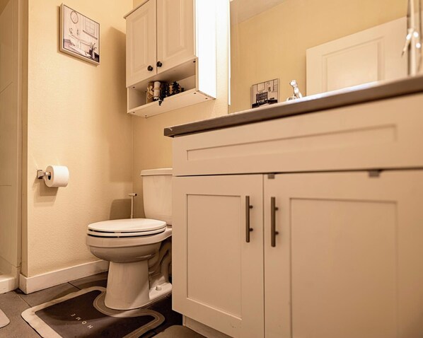 Een badkamer met een toilet, toiletpapier, een kast met spiegel en een plank met decoratieve objecten.