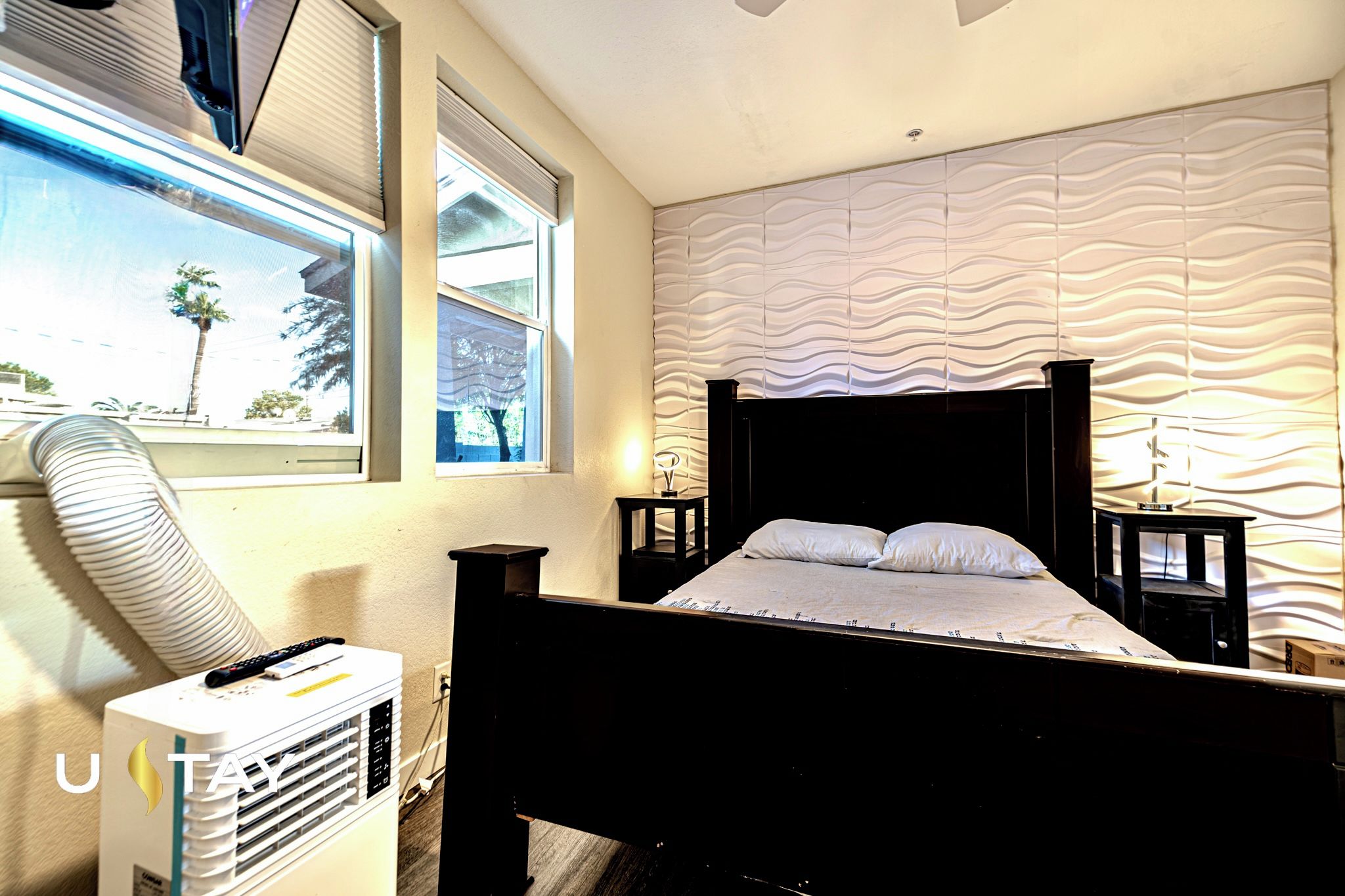 Un dormitorio con cama, ventana, aire acondicionado instalado en la pared y panel de pared texturizado.