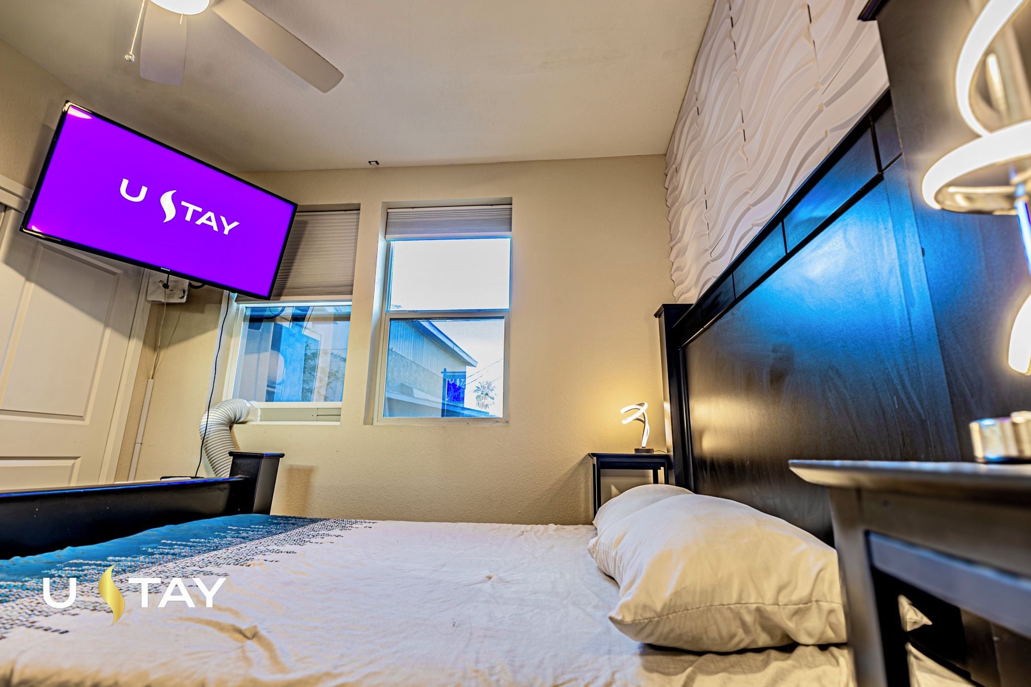 A hotel room with a bed, bedside tables, a desk, a chair, a window, and a wall-mounted TV.