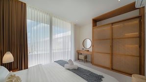 Quarto de hotel com uma cama grande, uma escrivaninha, um guarda-roupa e uma janela com cortinas leves.