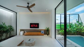 Un salon moderne avec un ventilateur de plafond, un logo Netflix, un canapé, une table basse et une vue sur une piscine.