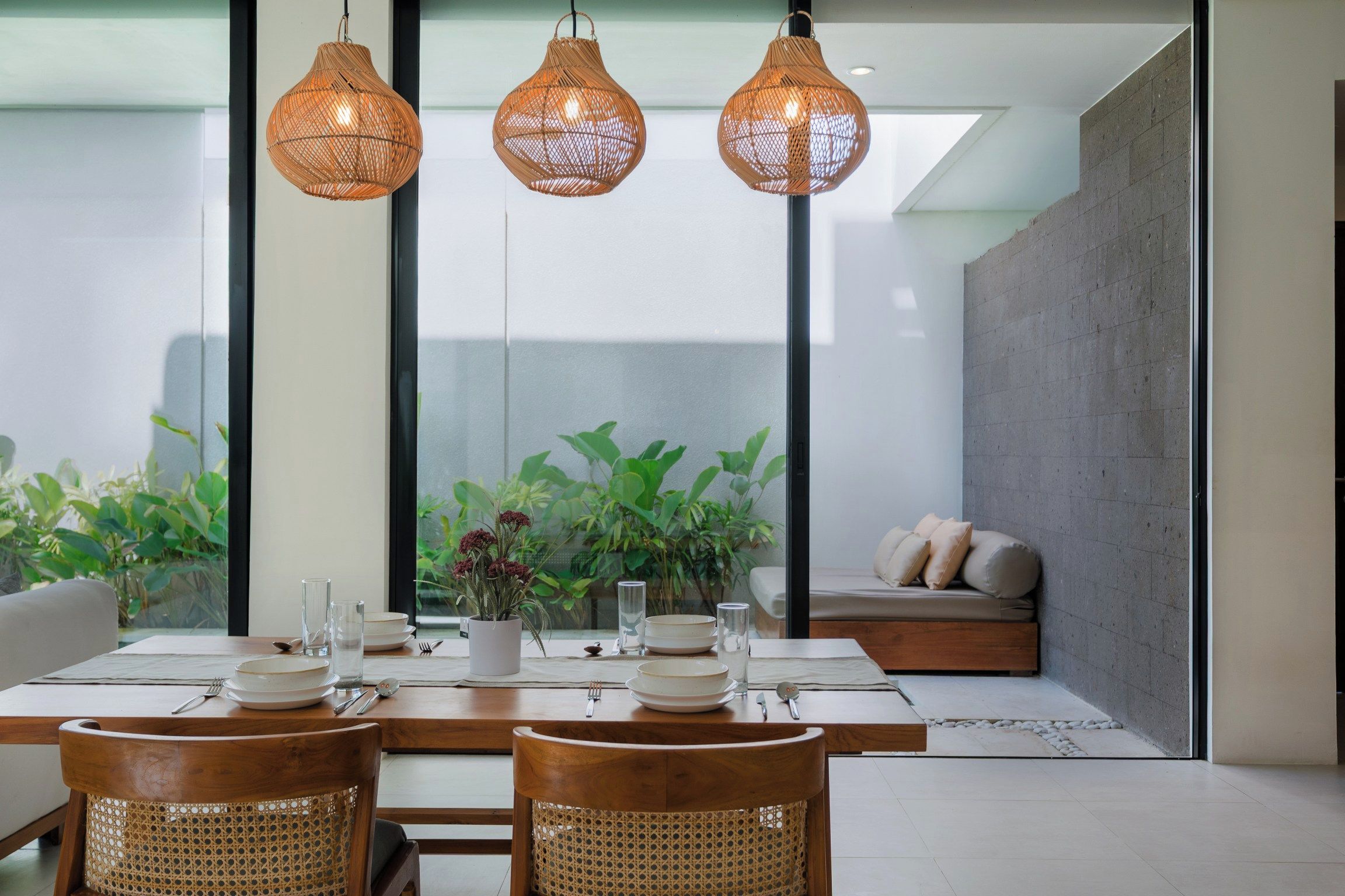 A dining area with a table set for four, surrounded by wicker chairs, and a seating area with a sofa and cushions.