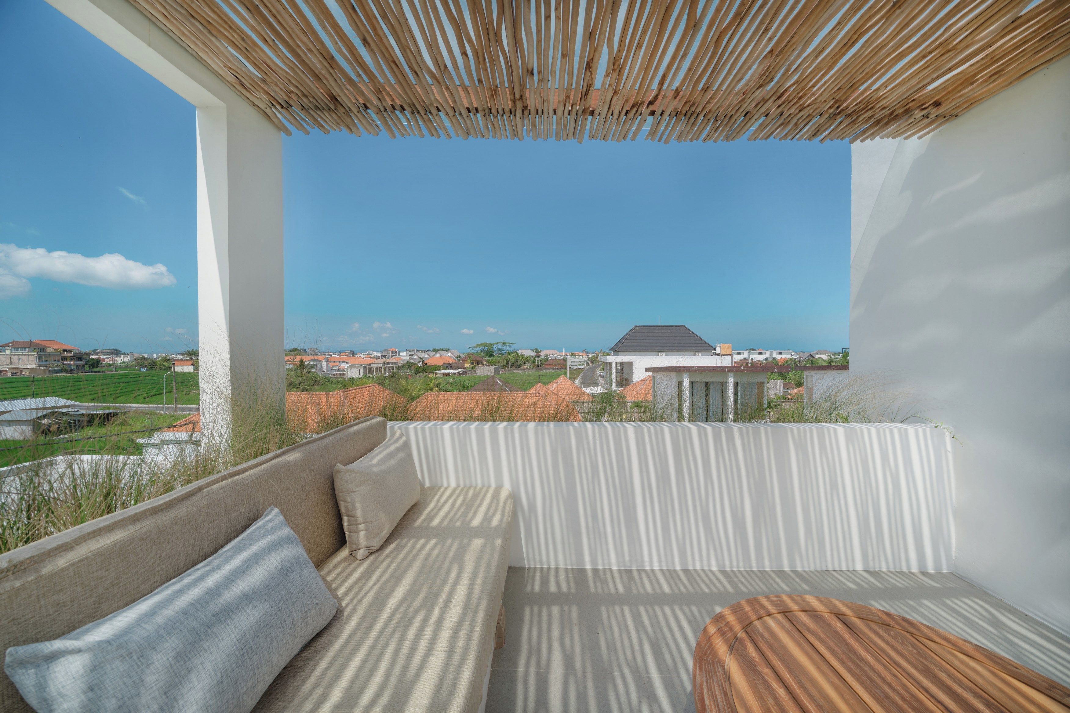 Un balcon donnant sur un quartier résidentiel, un mur blanc et une pergola en bois.