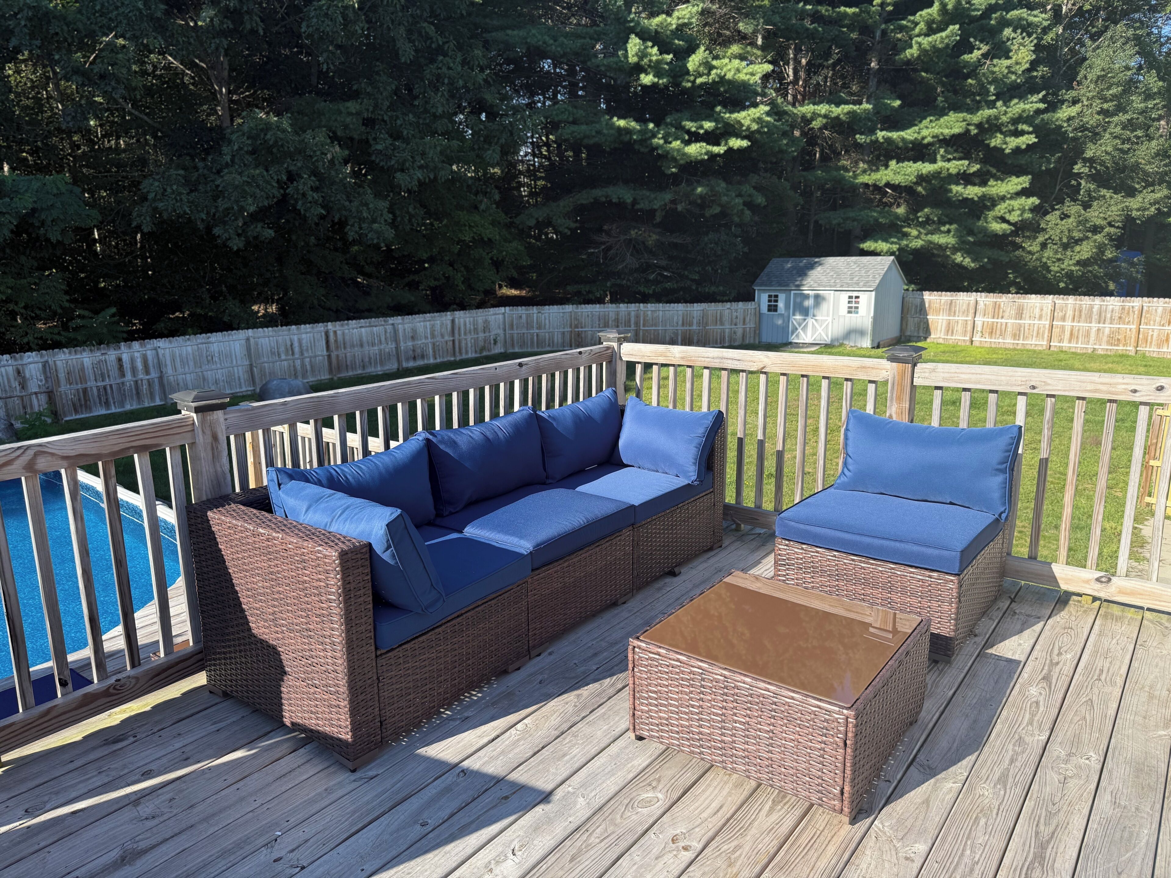 A deck with wicker furniture, a pool, and a wooden fence.