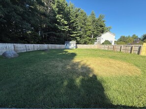 Ein Garten mit Holzzaun, einem Gartenhaus und einem Haus im Hintergrund.