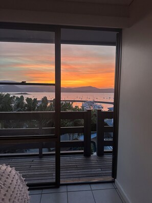 A balcony with a view of a sunset over water, featuring boats and distant hills. - Oceanview Villa, Airlie Beach (Airlie Beach)