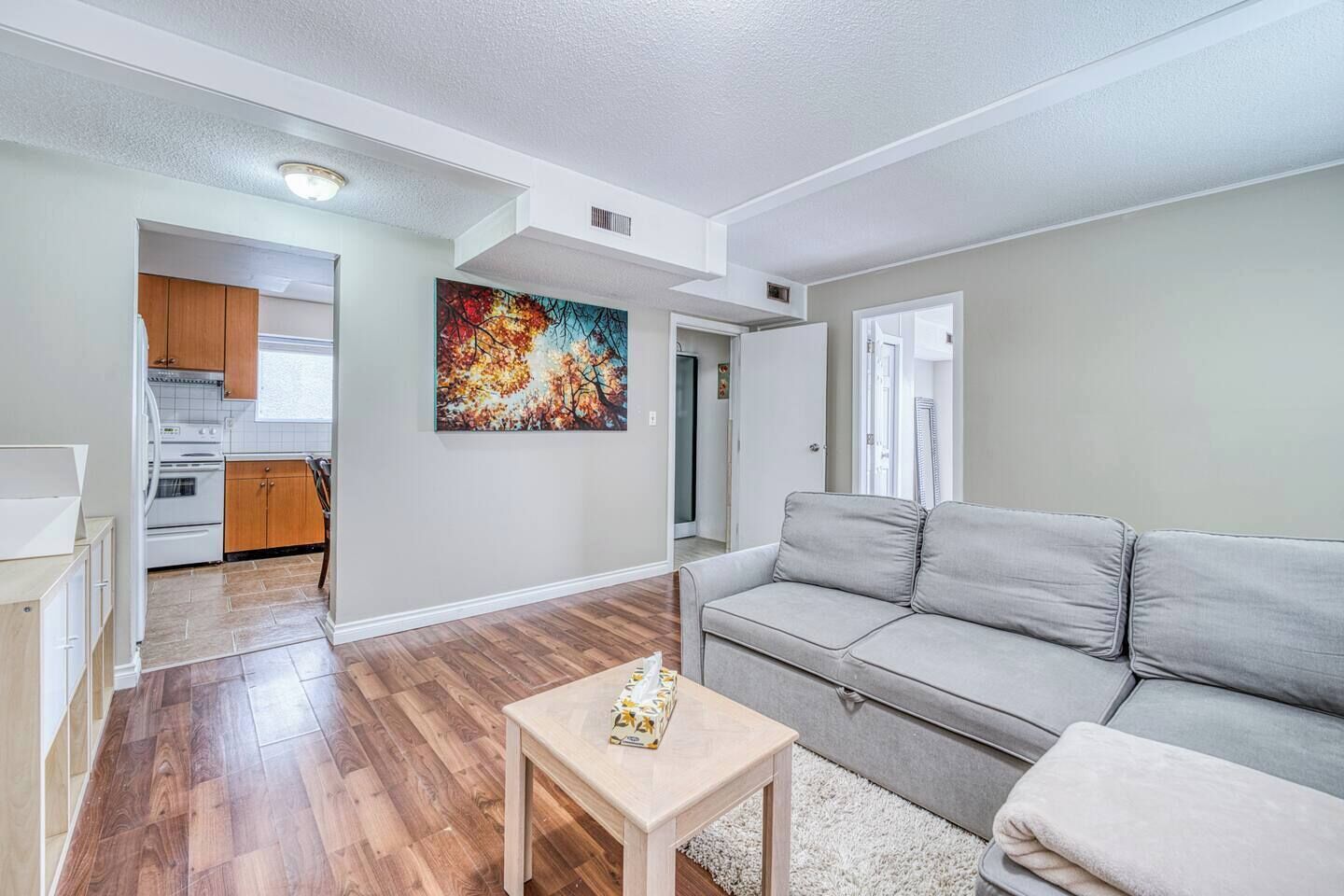Un salon moderne avec un canapé gris, une petite table en bois et un tableau coloré accroché au mur.