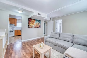 A modern living room with a grey sofa, a small wooden table, and a colorful painting on the wall. - Cozy Stay Near YVR | 1 Bed + Sofa Bed | Sleeps 4 (Vancouver)
