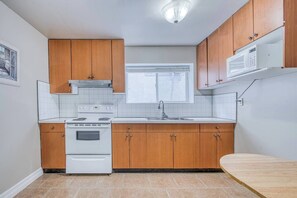 A compact kitchen with wooden cabinets, a white stove, and a microwave. - Cozy Stay Near YVR | 1 Bed + Sofa Bed | Sleeps 4 (Vancouver)
