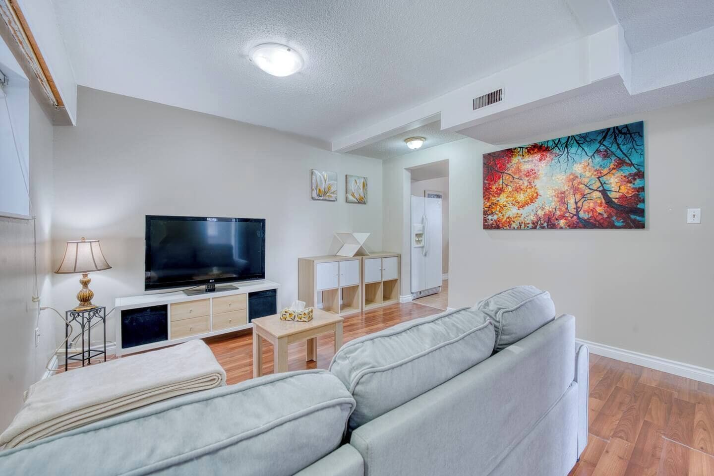 Un salon moderne avec un téléviseur à écran plat, un canapé, une table basse et un tableau accroché au mur.