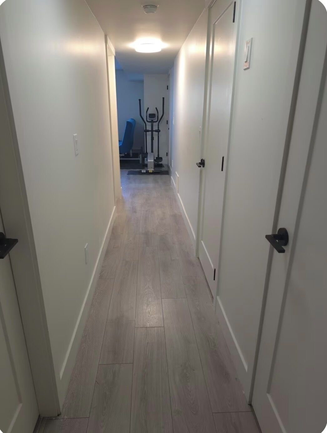 A hallway with a wooden floor, white walls, and a ceiling light.