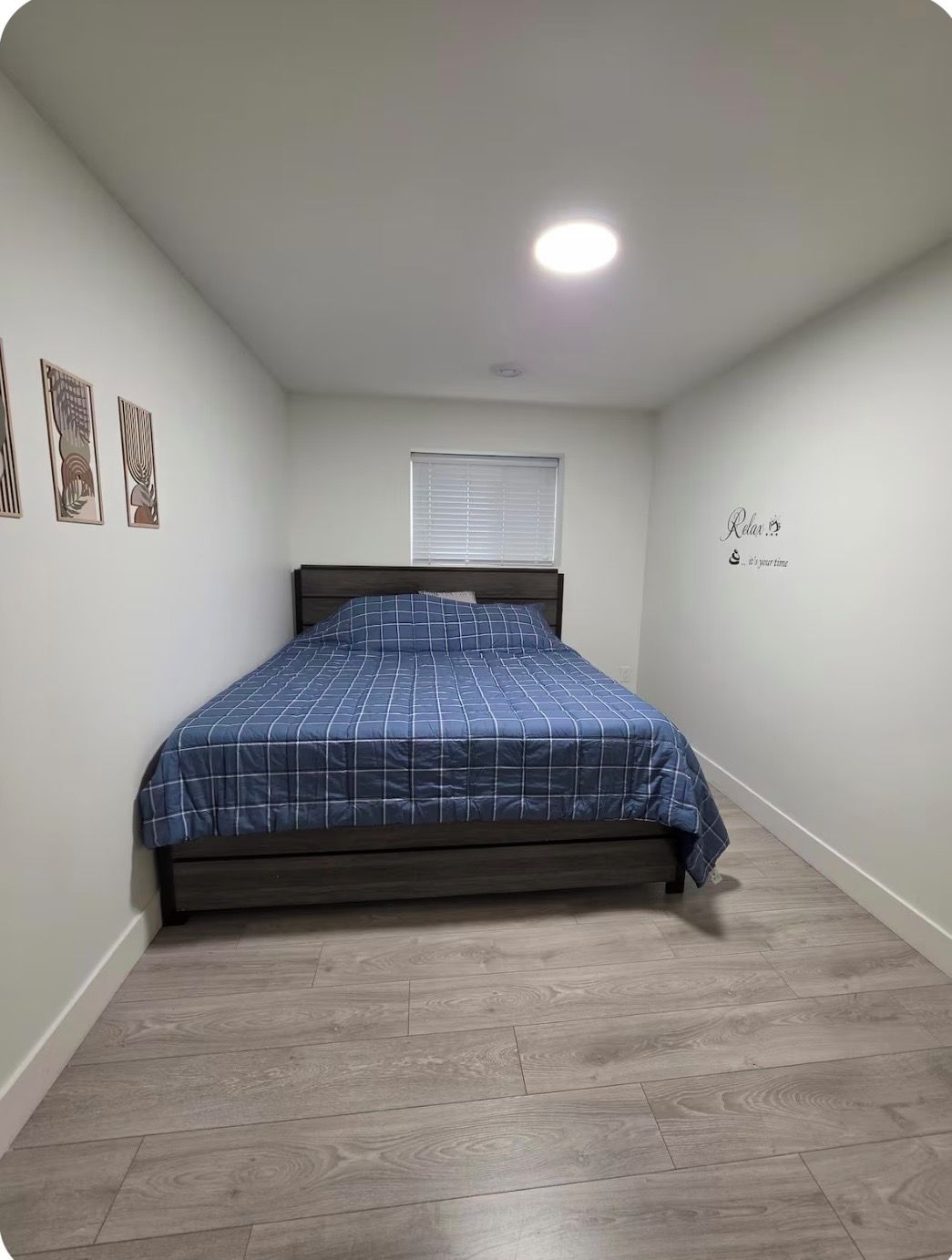 A bedroom with a bed, a window with blinds, and a wall with a motivational quote.
