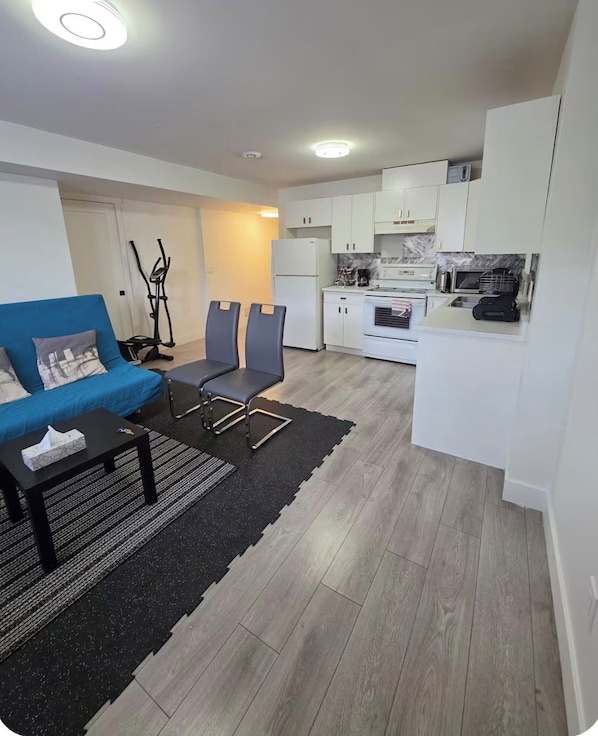 Un espacio habitable compacto con kitchenette, zona de comedor con mesa y sillas, y máquina de ejercicio.