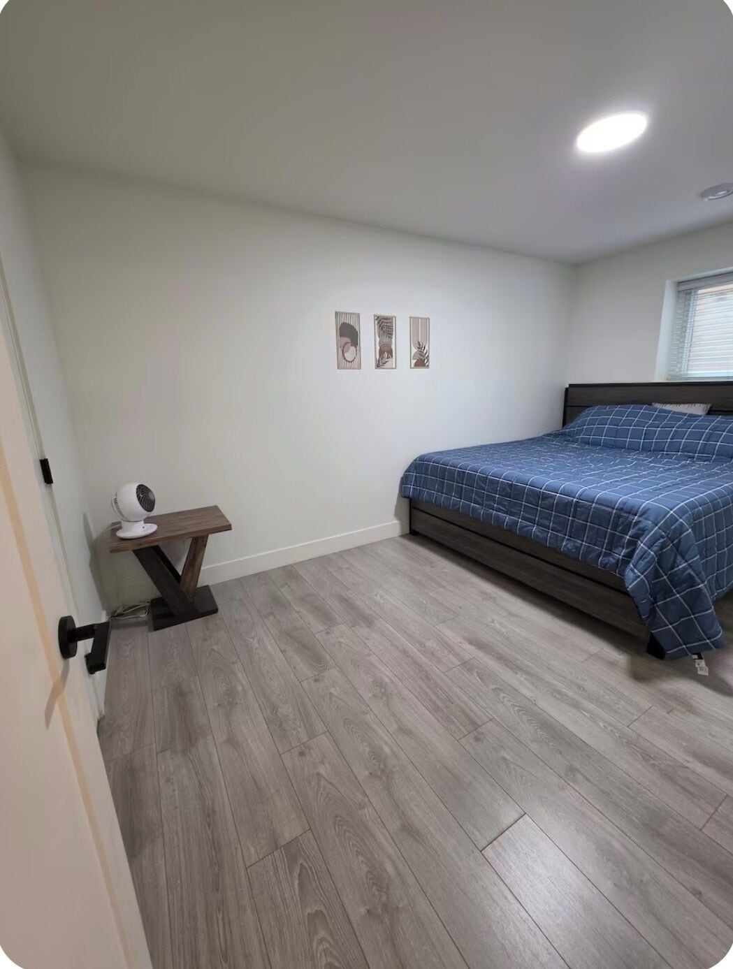 A bedroom with a bed, a bedside table with a lamp, and a wall-mounted fan.