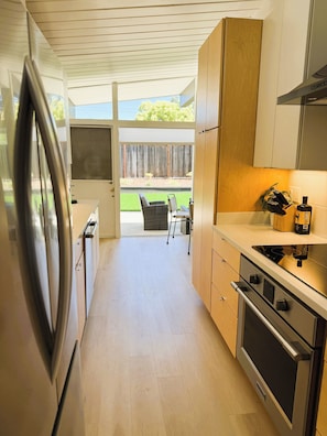 A modern kitchen with a built-in oven, a refrigerator, and a dining area with a table and chairs. - Modern Palo Alto Home -Perfect for Mid‑Term Stay (Palo Alto)