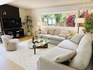 Uma sala de estar moderna com sofá seccional, mesa de centro de vidro, televisão de tela plana e planta em vaso.